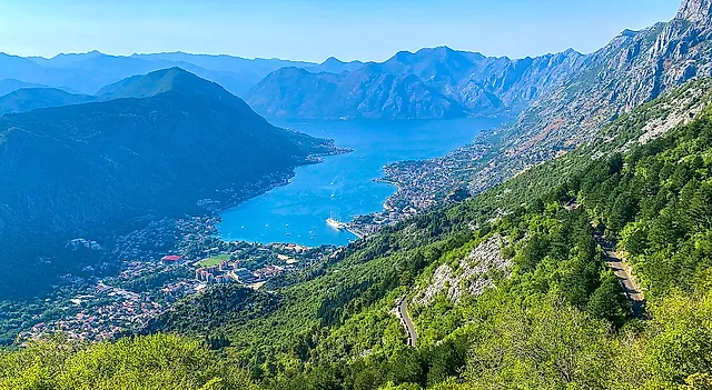 A road of hairpin bends on the green slope above Kotor, with the blue bay and the town below