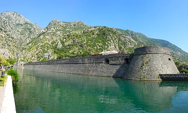 The city wall of Kotor along the Škurda river, with green water and a mountain slope behind