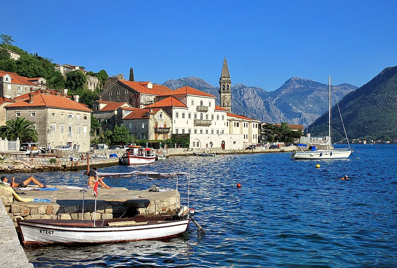 The waterfront of Perast with stone houses, red roofs and a bell tower, boats on the water
